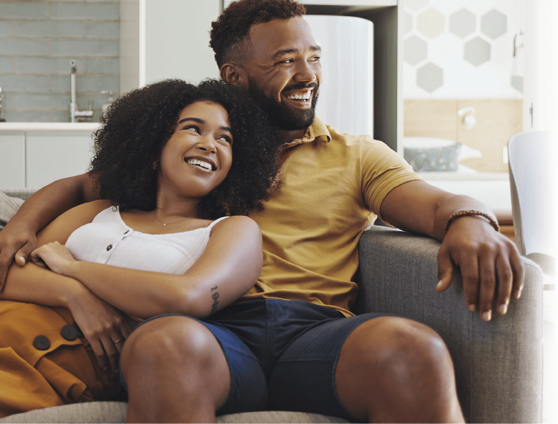 Couple daydreaming and cuddling on couch at home. Husband and wife sitting on sofa. Man embracing his female partner. Girlfriend and boyfriend laughing together. Man and woman thinking and bonding