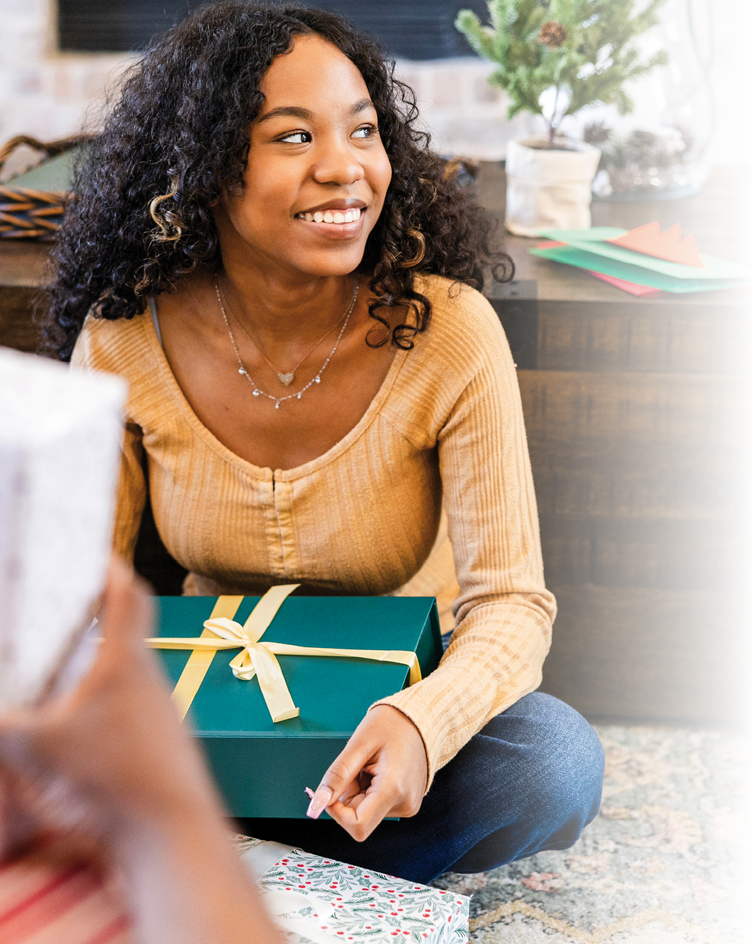 The smiling teenage girl looks at an unseen person while holding her Christmas gift in her lap.