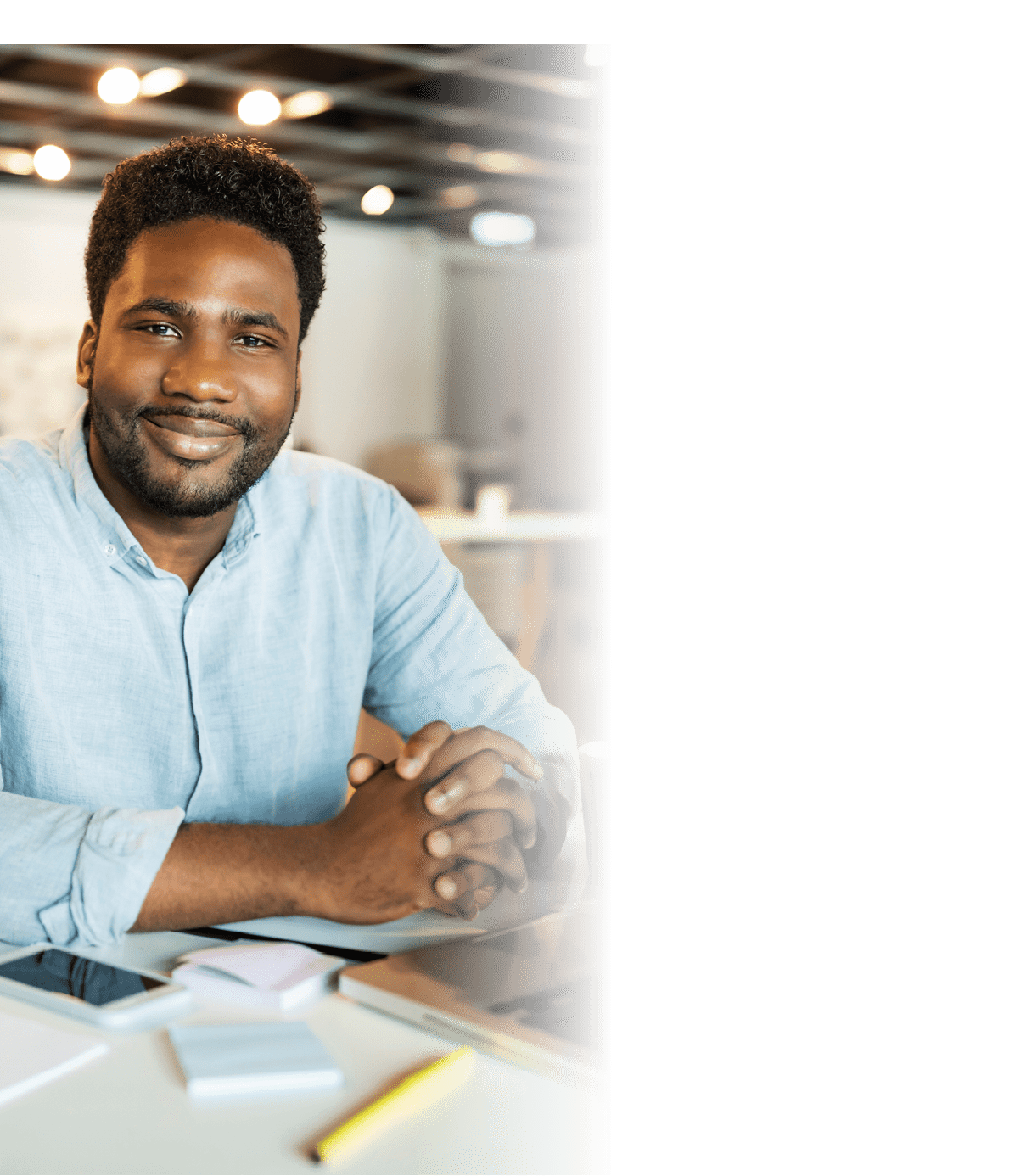 Young african-american man at his working place at the big office with other colleagues in the background
