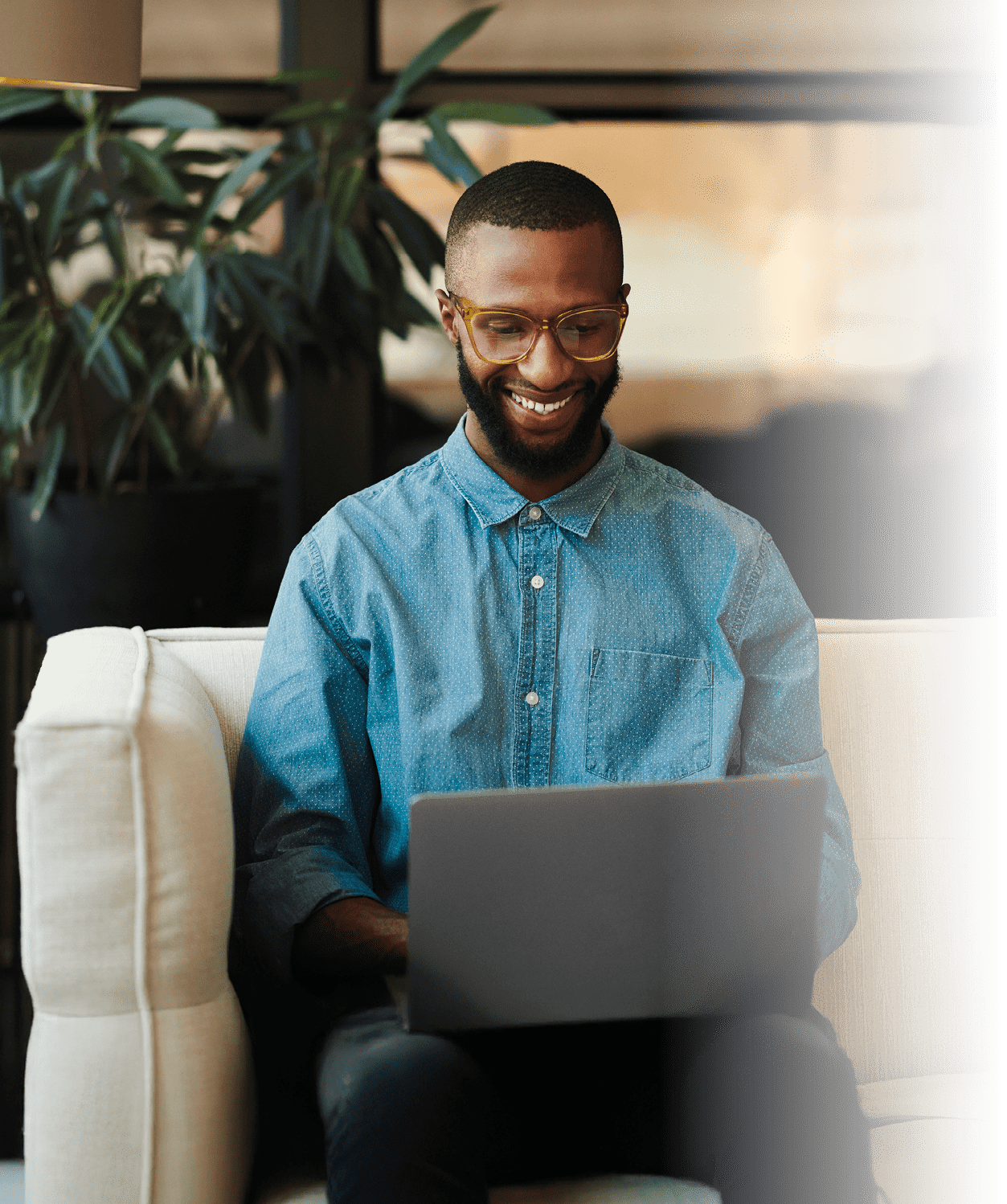 Happy freelancer wearing glasses with a laptop in the living room. A black man doing remote work on he's home sofa. Computer, small business and young male freelancer or entrepreneur working at home