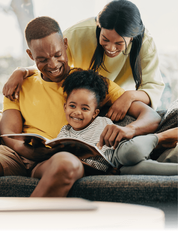 Happy little girl reading a story with her mother and father. Parents giving their child attention at home. Fun family moments on the weekend.