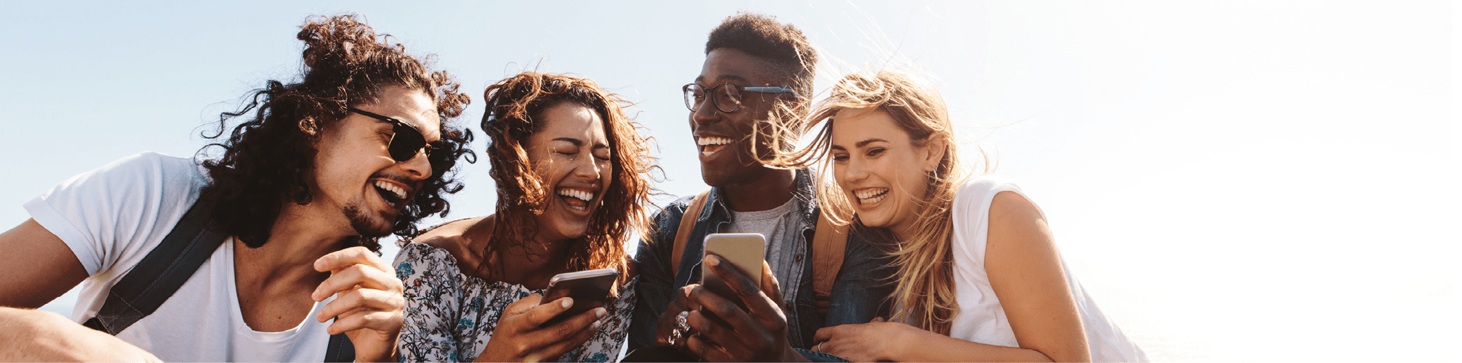 Young group of people sitting on top of mountain using smart phones and smiling. Diverse friends enjoying a day out.