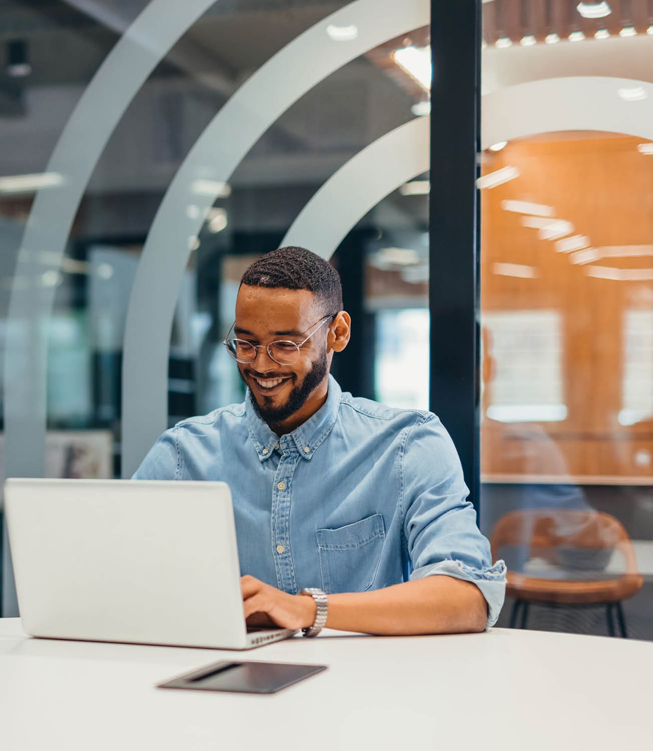 Portrait of cheerful young businessman working on his laptop in a co-working space. Modern businessman smiling while typing on his laptop. Happy entrepreneur sitting in an office.
