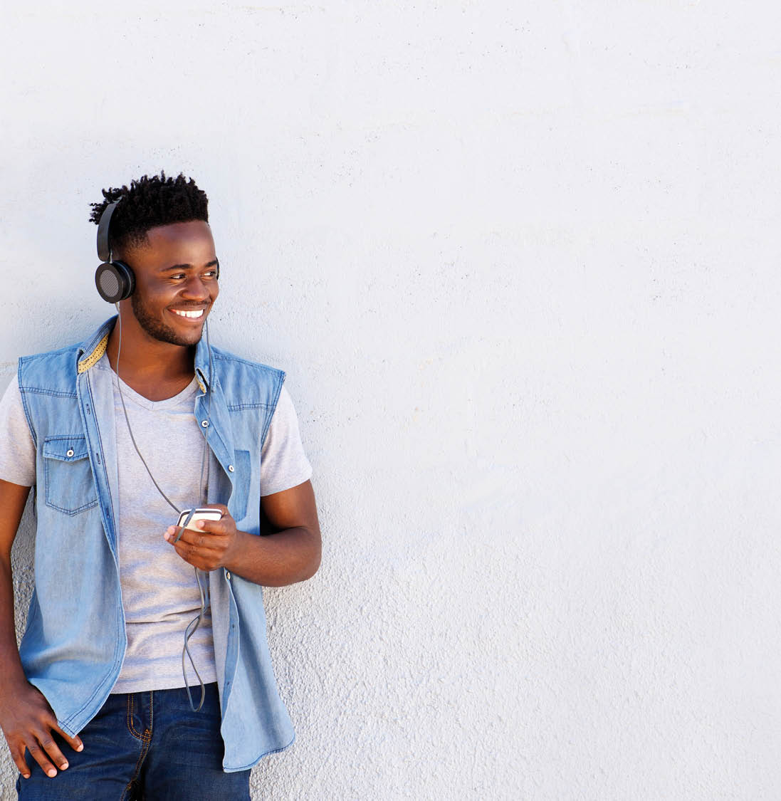 Portrait of smiling man with headphones and cellphone standing by white wall