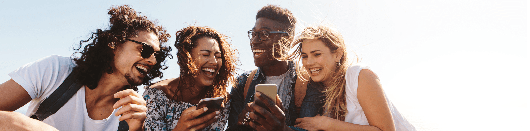 Young group of people sitting on top of mountain using smart phones and smiling. Diverse friends enjoying a day out.