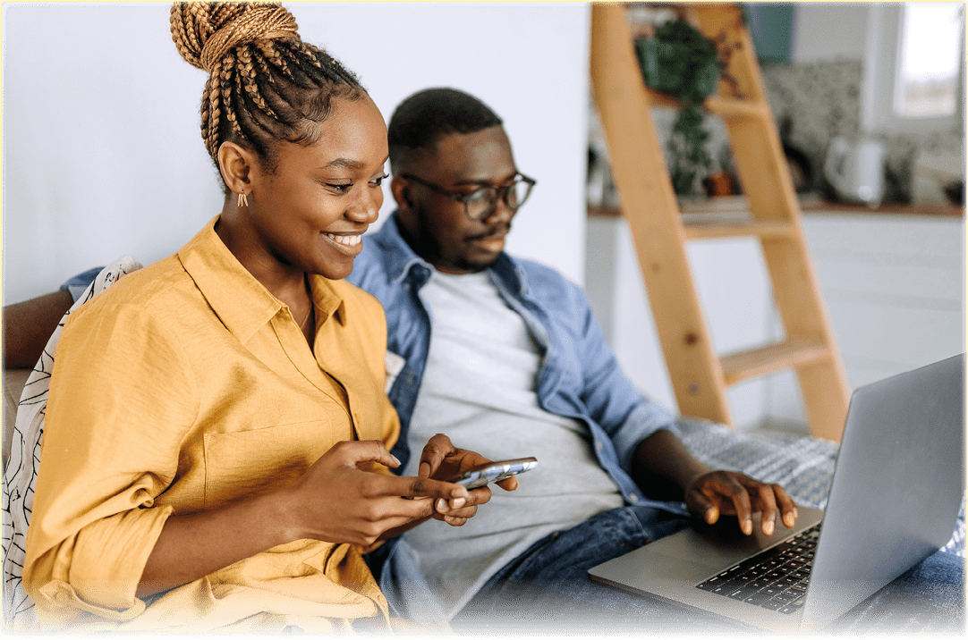 Young smiling couple shopping online at home, using laptop and smart phone